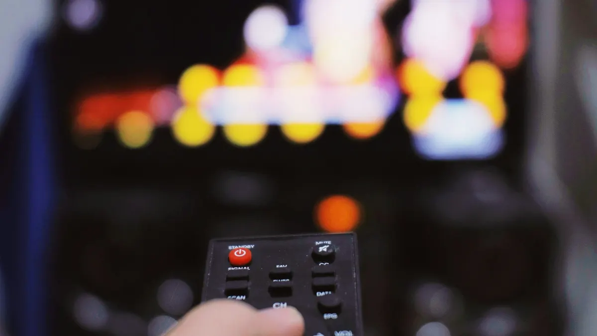 Amazon Fire TV Stick Fernbedienung in der Hand vor einem Fernsehbildschirm