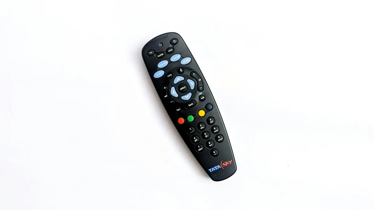 Kleine schwarze IPTV Set-Top-Box neben Fernbedienung vor einem Fernseher